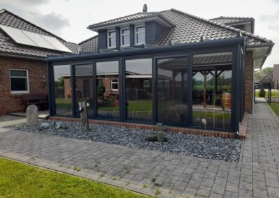 Wintergarten mit schwarzem Rahmen aus Aluminium und Glasfront an einem Backsteinhaus.