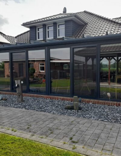 Wintergarten mit schwarzem Rahmen aus Aluminium und Glasfront an einem Backsteinhaus.